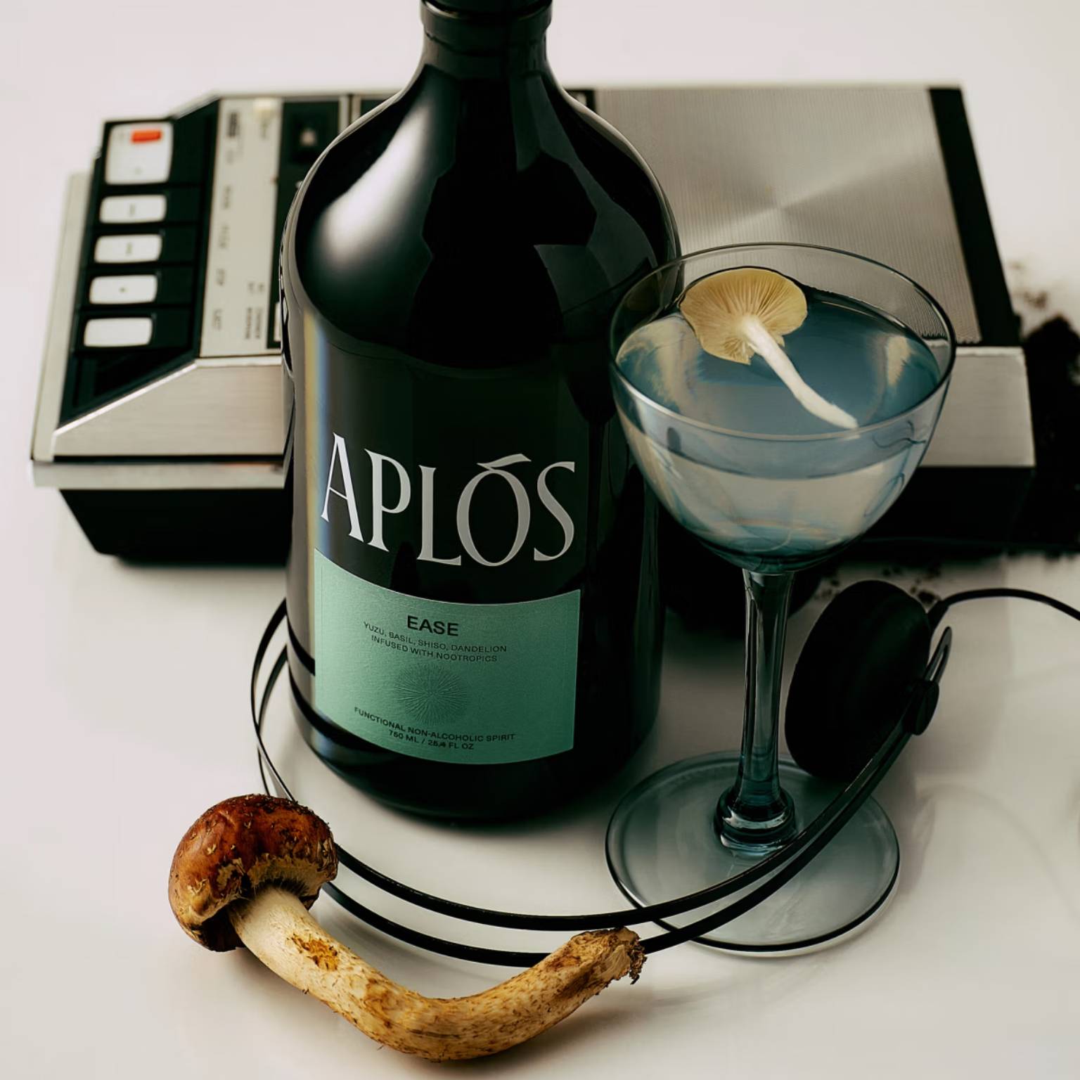 A bottle of the nonalcoholic spirit "Aplos Ease" with lion's mane mushroom, headphones, and a martini glass.