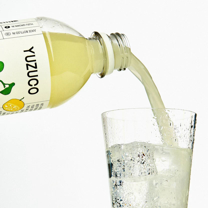 Yuzu juice being poured from a bottle labeled 'YUZUCO' into a glass with ice.